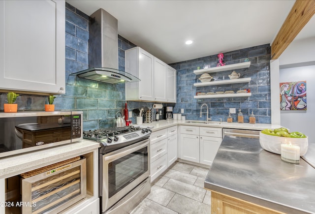 kitchen with stainless steel counters, appliances with stainless steel finishes, sink, wall chimney exhaust hood, and white cabinets