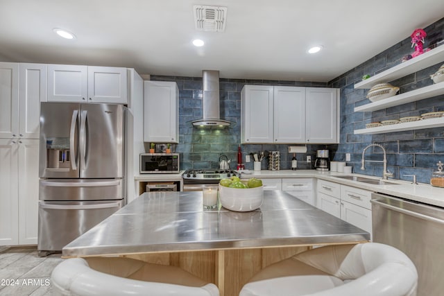 kitchen with stainless steel counters, appliances with stainless steel finishes, wall chimney range hood, sink, and white cabinetry