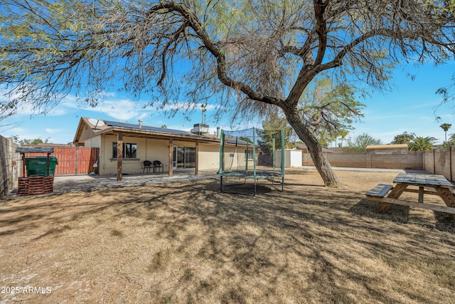 back of property with a patio, a trampoline, a fenced backyard, a yard, and solar panels