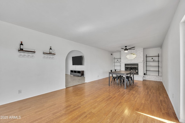 dining space featuring a ceiling fan, wood finished floors, a fireplace, and arched walkways