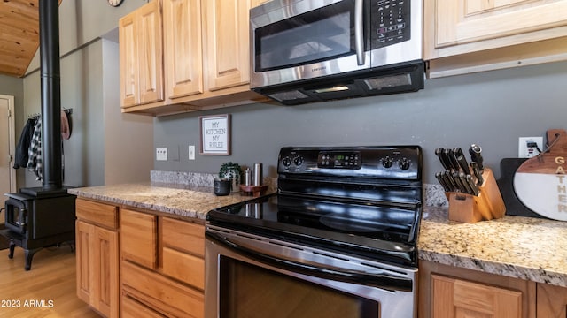 kitchen featuring black electric range oven, light hardwood / wood-style flooring, light stone counters, and a wood stove