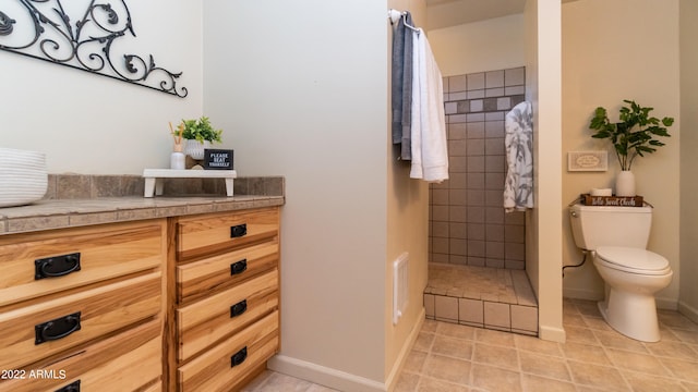 bathroom with vanity, toilet, a tile shower, and tile patterned flooring