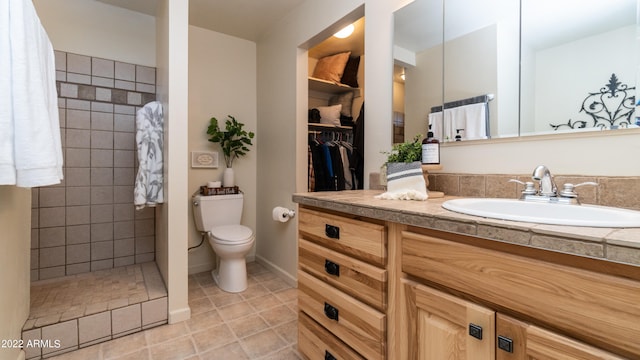 bathroom with vanity, toilet, a tile shower, and tile patterned flooring