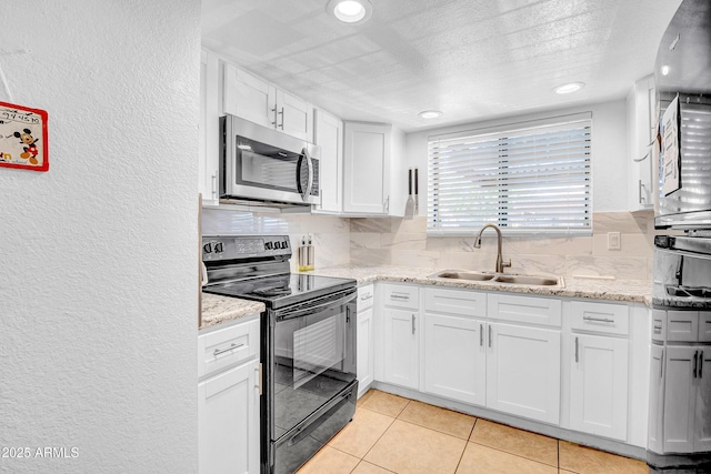 3027 E Grandview Rd Unit 1, Phoenix, AZ 85032 - kitchen featuring stainless steel microwave, black range with electric stovetop, a textured wall, decorative backsplash, and white cabinets