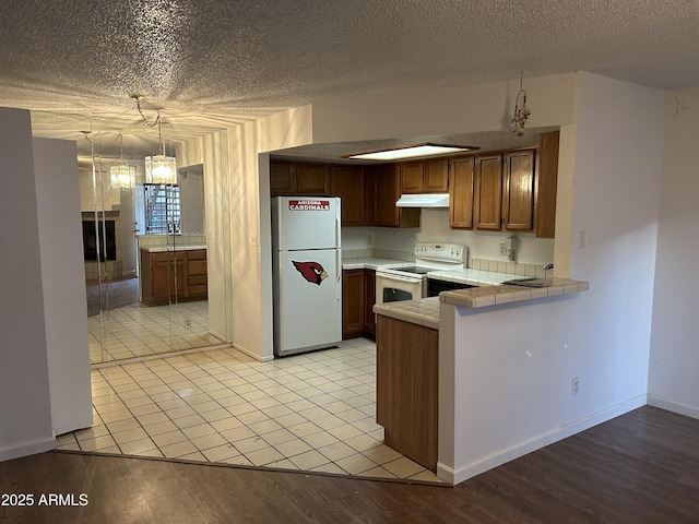 kitchen with tile counters, light wood-style floors, a peninsula, white appliances, and under cabinet range hood