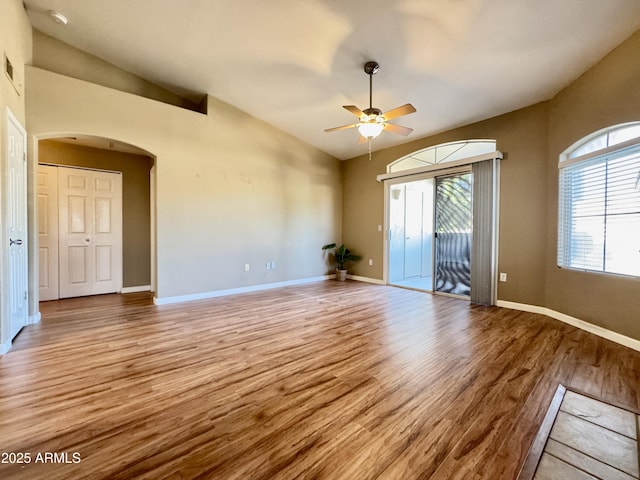 spare room with light wood-type flooring, arched walkways, ceiling fan, and a healthy amount of sunlight