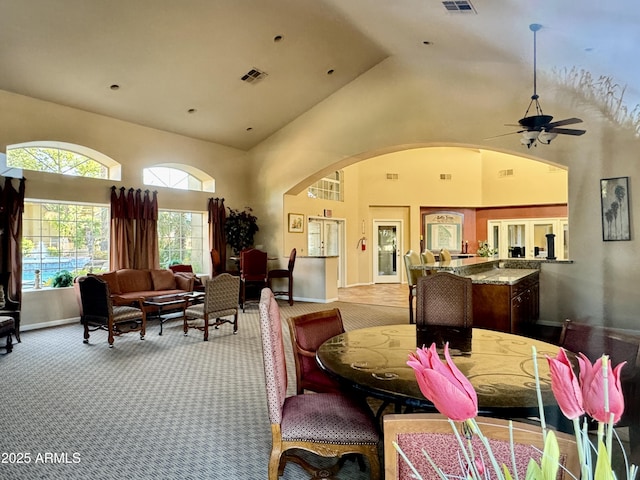 carpeted dining space with ceiling fan, visible vents, arched walkways, high vaulted ceiling, and baseboards