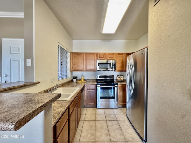 kitchen with brown cabinets, a sink, a textured wall, stainless steel appliances, and light tile patterned flooring