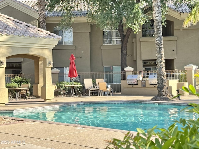 community pool with area for grilling, exterior kitchen, fence, and a patio area