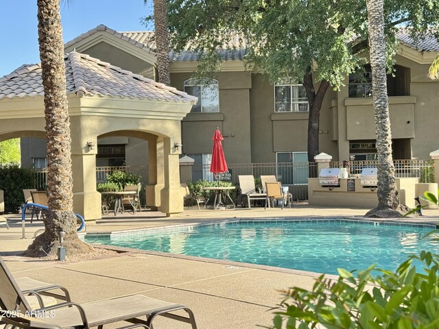 pool with fence, a gazebo, exterior kitchen, a patio area, and a grill