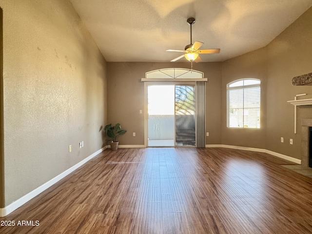 empty room with baseboards, a ceiling fan, wood finished floors, and a fireplace