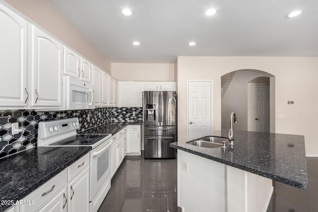 kitchen with sink, white appliances, white cabinetry, dark stone countertops, and a center island with sink