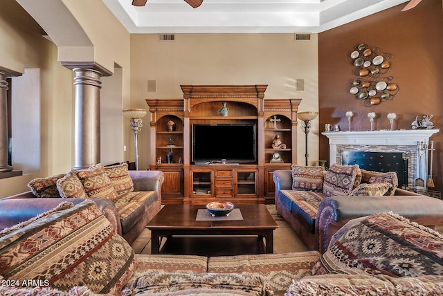 living room featuring decorative columns, a raised ceiling, ceiling fan, a tile fireplace, and tile patterned flooring