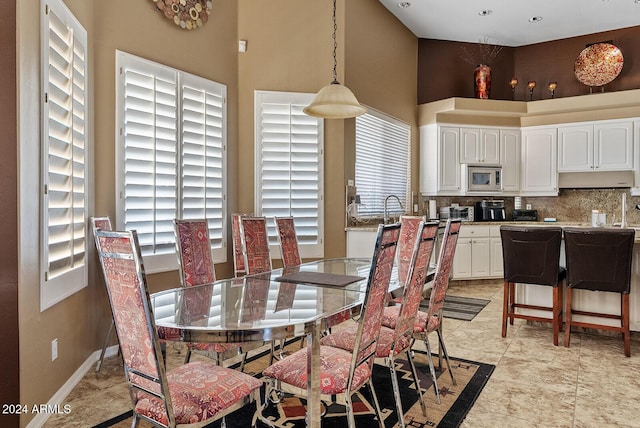 tiled dining area featuring a towering ceiling, plenty of natural light, and sink