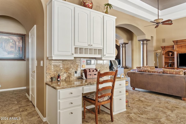 kitchen with light stone countertops, white cabinetry, ornate columns, and ceiling fan