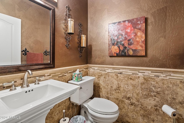 bathroom with toilet, tile walls, and sink