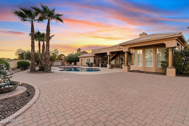 pool at dusk featuring a patio area and a hot tub