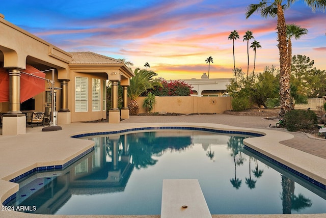 pool at dusk featuring a patio and a diving board