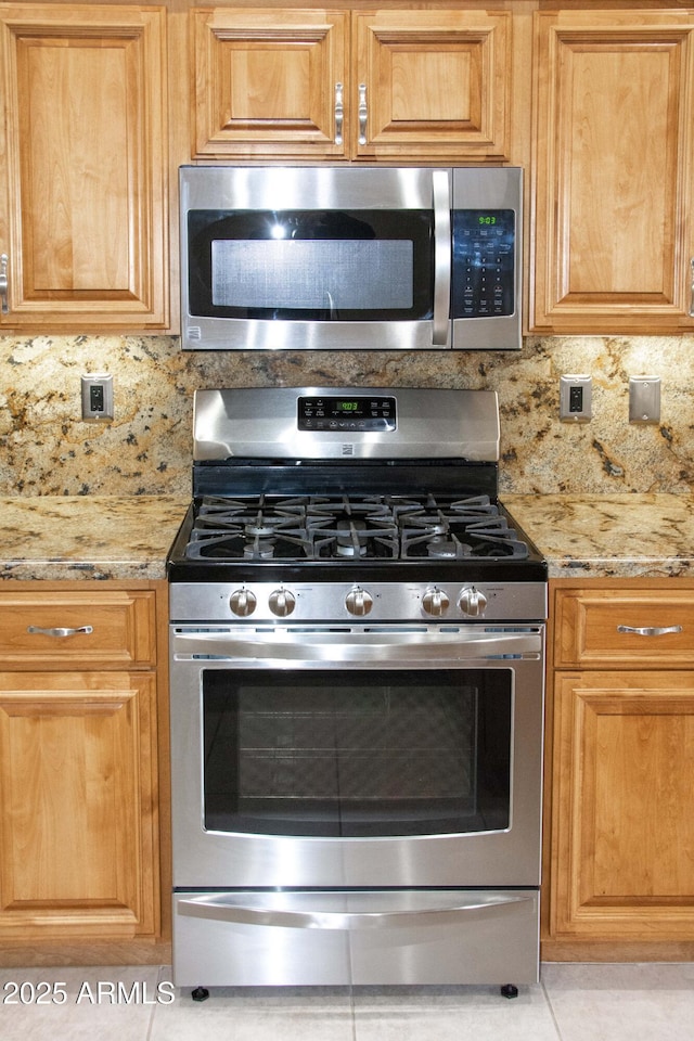 kitchen with light stone countertops, backsplash, stainless steel appliances, and light tile patterned floors