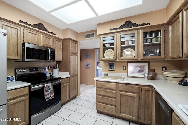 kitchen with stainless steel appliances, light countertops, glass insert cabinets, and visible vents