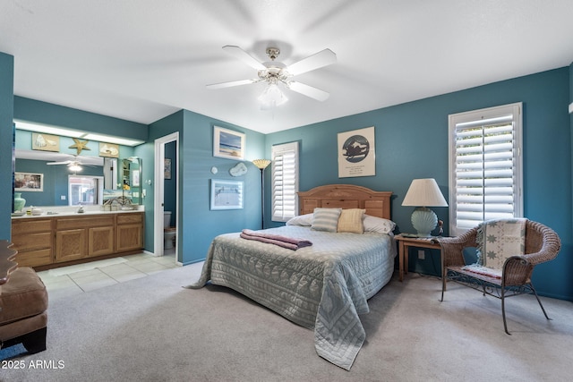 bedroom with light tile patterned floors, ceiling fan, ensuite bathroom, light colored carpet, and a sink