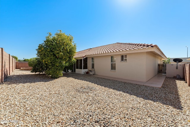 rear view of property featuring stucco siding, a fenced backyard, a gate, and a tiled roof