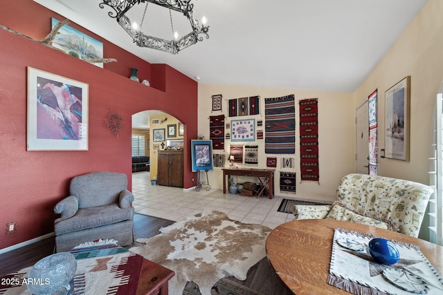 living area featuring arched walkways, a notable chandelier, light tile patterned floors, vaulted ceiling, and baseboards