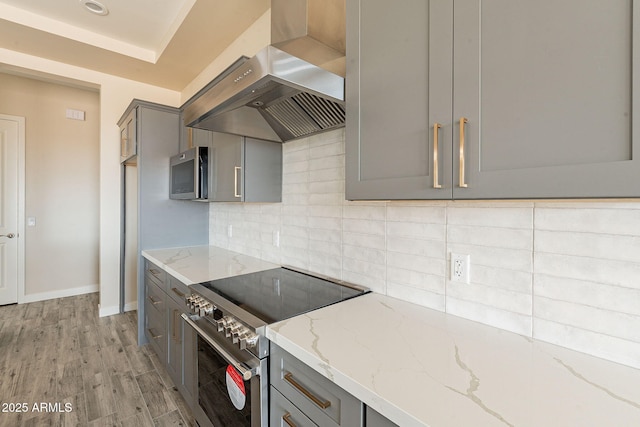 kitchen featuring tasteful backsplash, stainless steel appliances, light wood-style flooring, wall chimney exhaust hood, and gray cabinetry