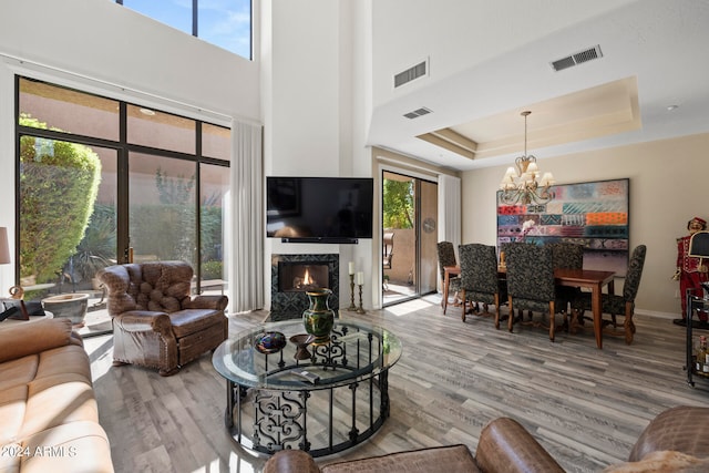 living room with hardwood / wood-style flooring, a high end fireplace, a raised ceiling, and a chandelier