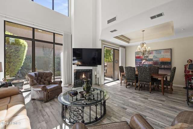 living room featuring hardwood / wood-style flooring, a high end fireplace, a raised ceiling, and an inviting chandelier