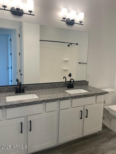 bathroom featuring double vanity, wood finished floors, toilet, and a sink