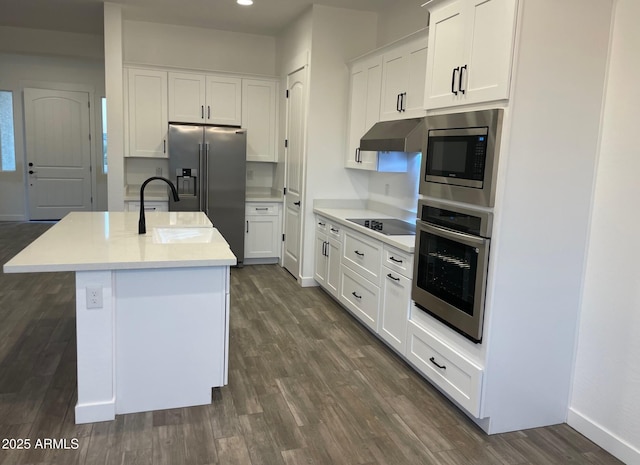 kitchen with dark wood-type flooring, a center island with sink, under cabinet range hood, stainless steel appliances, and white cabinets