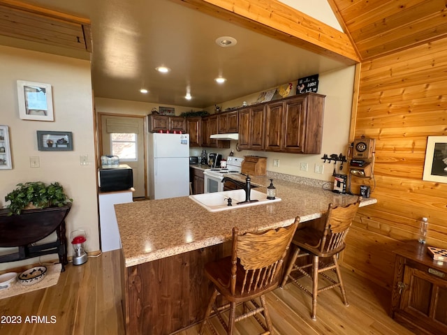 kitchen featuring white appliances, wood walls, light wood-type flooring, kitchen peninsula, and vaulted ceiling