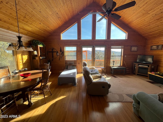 living room featuring wood walls, hardwood / wood-style floors, high vaulted ceiling, and ceiling fan with notable chandelier