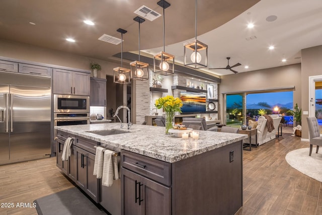 kitchen with dark brown cabinetry, built in appliances, hanging light fixtures, and sink