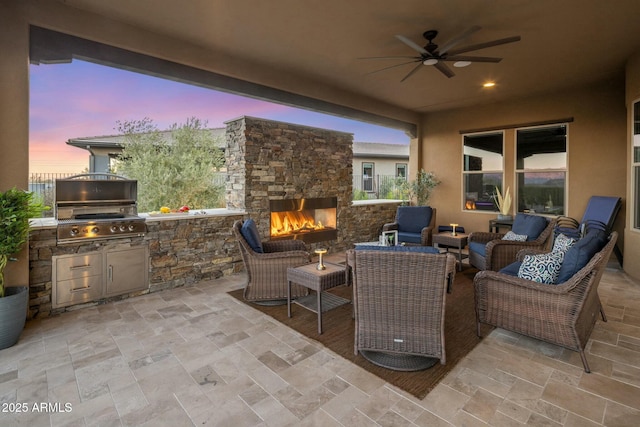 patio terrace at dusk featuring an outdoor living space with a fireplace, ceiling fan, exterior kitchen, and grilling area