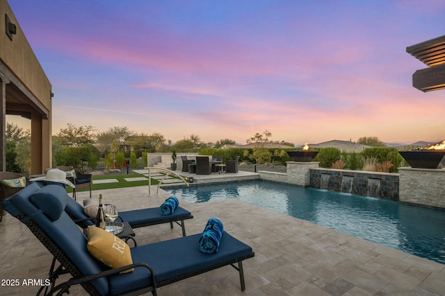 pool at dusk featuring pool water feature and a patio area