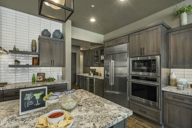 kitchen with built in appliances, dark brown cabinetry, and backsplash