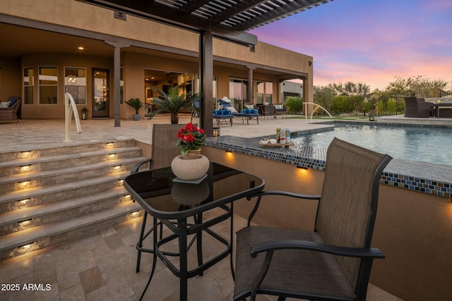 pool at dusk featuring a pergola, pool water feature, and a patio area