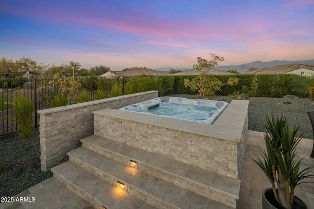 pool at dusk with a mountain view and an outdoor hot tub