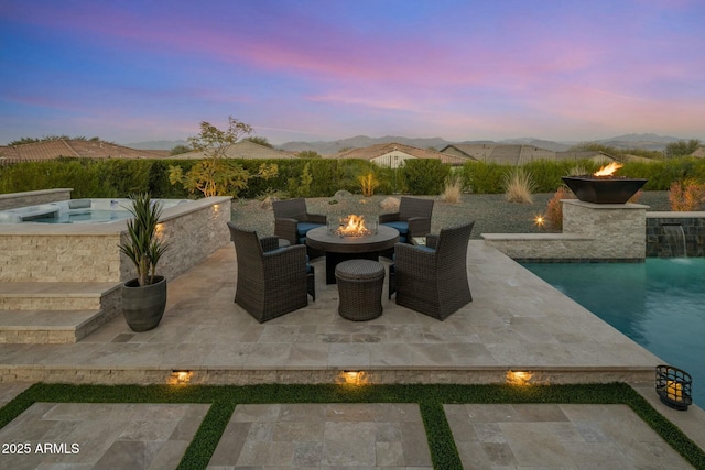 patio terrace at dusk with pool water feature, a mountain view, and an outdoor fire pit