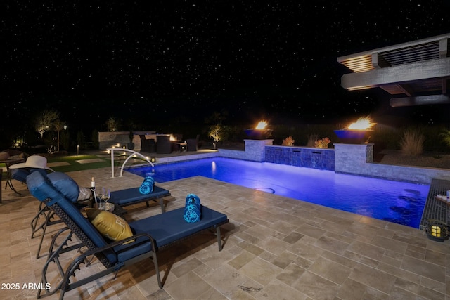 pool at night featuring pool water feature and a patio area