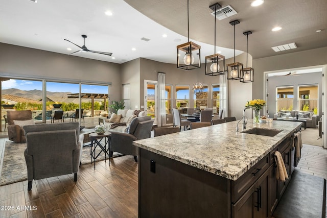 kitchen featuring ceiling fan with notable chandelier, sink, decorative light fixtures, a center island with sink, and a mountain view