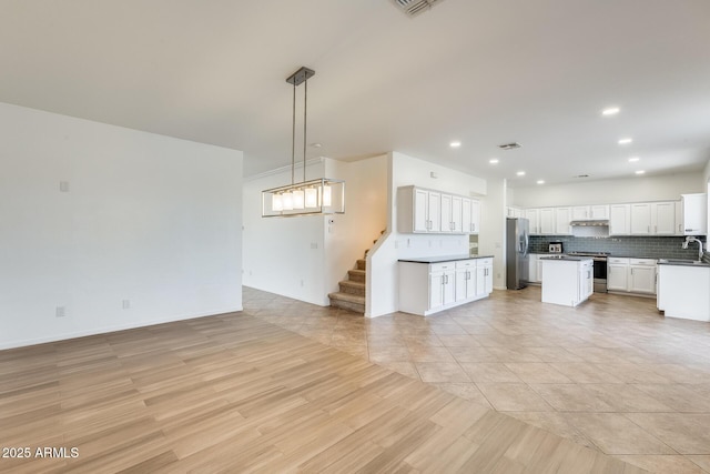 kitchen with stainless steel appliances, a kitchen island, white cabinets, decorative light fixtures, and light tile patterned floors