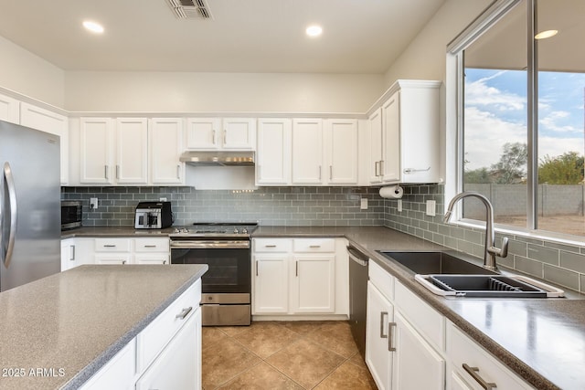 kitchen with sink, stainless steel appliances, light tile patterned floors, decorative backsplash, and white cabinets