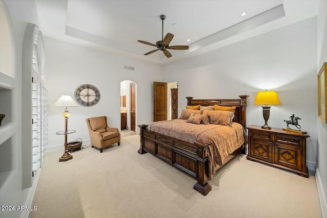 carpeted bedroom featuring a raised ceiling, ceiling fan, ensuite bathroom, and a high ceiling