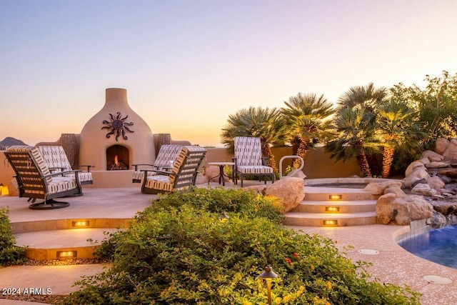 patio terrace at dusk featuring an outdoor fireplace