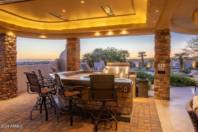 patio terrace at dusk featuring a grill, exterior bar, and an outdoor kitchen