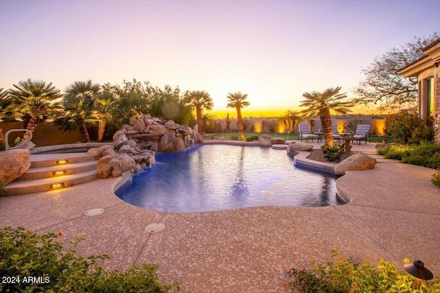 pool at dusk with a jacuzzi, a patio, and pool water feature