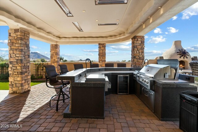 view of patio featuring wine cooler, an outdoor kitchen, grilling area, a mountain view, and a bar